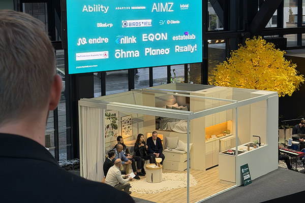 Panelsamtale i et glassrom på scenen under Oslo Proptech Summit 2026, med en storskjerm som viser utstillerne, blant dem Clevio og ERV.